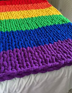 a crocheted rainbow blanket on top of a bed