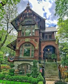 an old victorian house with many windows and steps leading up to the front door, surrounded by lush greenery