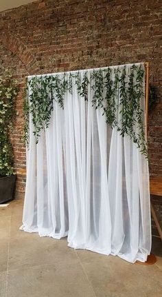 a white curtain with green plants on it in front of a brick wall and bench