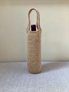 a woven bag with a bottle in it on a table next to a white wall