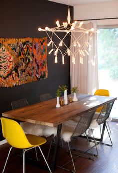 a dining room table with yellow chairs in front of a painting on the wall above it