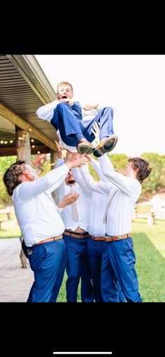 a group of men in white shirts and blue pants holding a young boy on his back