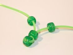 three green beads are attached to a cord on a white surface, with one bead in the middle