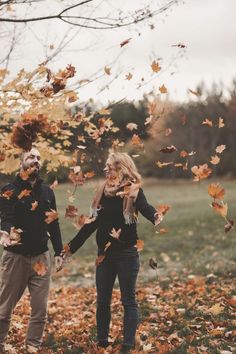 a man and woman holding hands while standing in leaves