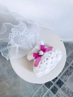 a white plate topped with a crocheted hat and pink ribbon on top of a tiled floor