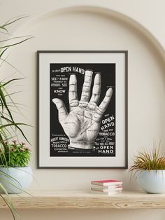 an open hand poster hangs on the wall above a shelf with potted plants and books