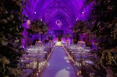 an indoor wedding venue with purple lighting and floral arrangements on either side of the aisle