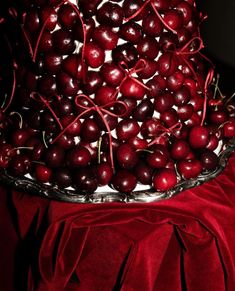 a cake with cherries on it sitting on a red cloth covered tablecloth next to a bowl of cherries