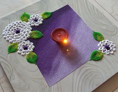 a lit candle sitting on top of a purple mat with white flowers and green leaves