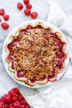 raspberry pie with crumbled crust on top and fresh raspberries scattered around