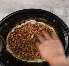 a person placing pecans on top of a pie crust in a black crock pot