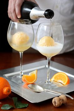 a person pouring wine into two glasses on a tray with oranges and garlic next to it