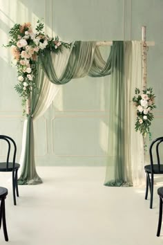 two black chairs are sitting in front of an arch decorated with flowers and greenery