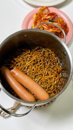 two hot dogs and some noodles in a pot on a stove top with other food items