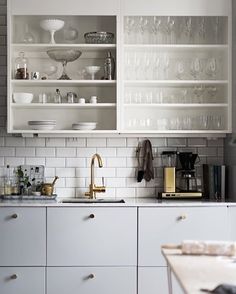 a kitchen with white cabinets and glassware on the counter top, including wine glasses