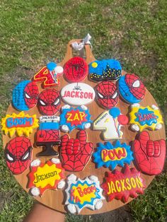 a person holding up a wooden board with decorated cookies on it in the shape of superheros