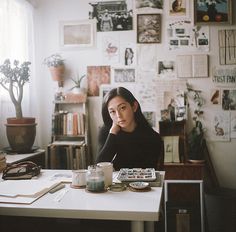 a woman sitting at a table in front of a wall with pictures and paintings on it