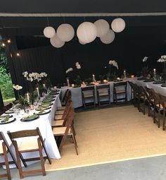 a table set up for an event with white flowers and paper lanterns hanging from the ceiling