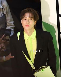 a young man wearing a suit and holding a green purse