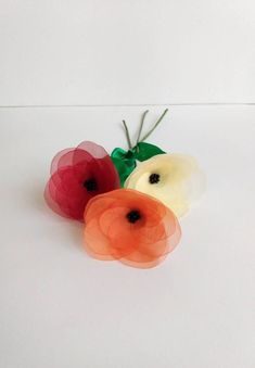 three different colored flowers on a white surface