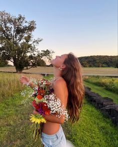 a woman standing in the grass with her back to the camera and holding some flowers