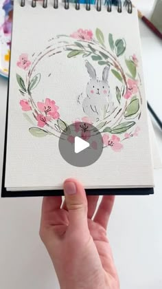 a hand holding a spiral notebook with an image of a bunny in the center and flowers around it