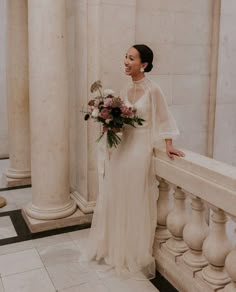 a woman in a wedding dress standing next to columns and holding a bouquet with flowers