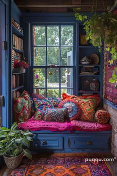 a window seat with colorful pillows on it in front of a bookshelf and potted plants