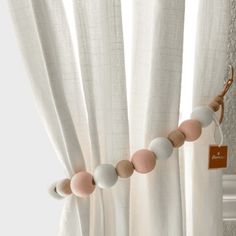 a white curtain with pink and grey beads hanging from it's side next to a window