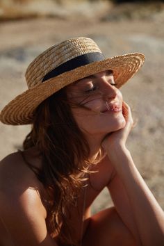 a woman wearing a straw hat sitting on the beach