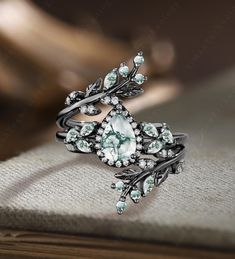 a close up view of a ring with green stones and leaves on the front, sitting on top of a book