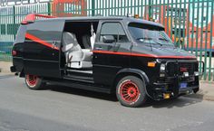 a black van with red trim parked in front of a fence