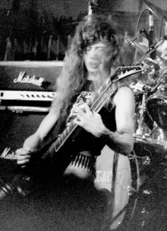 a man with long hair holding a guitar in front of a recording equipment set up