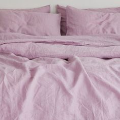 an unmade bed with pink linens and pillows on top of it, in front of a white wall