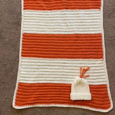 an orange and white crocheted blanket on the floor with a drawstring bag