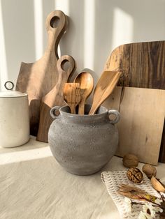 a table topped with wooden utensils and cutting boards next to a vase filled with wood spoons