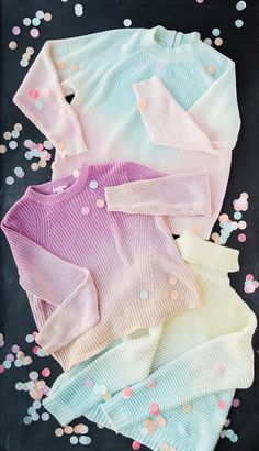 three baby sweaters laying on top of confetti