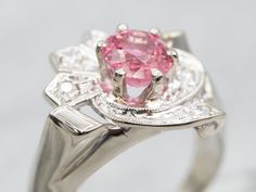 A beautiful sparkling bright pink tourmaline adorns the center of this fantastic 1950s cocktail ring! The center gemstone is surrounded by sweeping ribbons, connected by a swirling tapered metal diamond-studded design engraved with retro motifs, which gives the ring a sense of movement! With lovely little cut-outs in between the designs and plenty of sparkles, this definitely makes for one unique and beautiful cocktail ring!Metal: 14K White GoldGem: Pink Tourmaline 1.36 CaratsGem Measurements: 6.3 mm, RoundAccents: 6 Diamonds totaling .17 Carats, SI in Clarity, H-I in ColorRing Size: 7.75Marks: "14K" Stamped on the inside band Vintage Pink Rings For Anniversary, Retro Pink Jewelry For Formal Occasions, Pink Retro Style Jewelry For Formal Occasions, Pink Art Deco Rings For Anniversary, Antique Pink Diamond Rings, Antique Pink Rings With Center Stone, Pink Brilliant Cut Fine Jewelry, Vintage Pink Brilliant Cut Rings, Art Deco Pink Wedding Ring