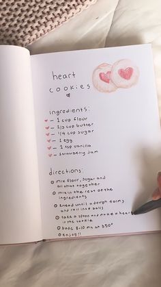 someone is holding a pen and looking at a recipe book with hearts on the pages