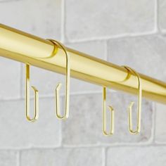 three hooks are hanging on the side of a metal rail against a white brick wall