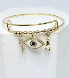 Bracelet is 18k Gold plated Stainless steel with ball spacer beads. Bracelet is 60mm, 1.5mm thickness, and expands to desired fit. Horn charm is Covered front and back In Micro Pave Cubic Zirconia and is 5x17mm. Evil Eye is 21X13mm Micro pave and white enamel. Hand charm is Gold Plated Stainless steel 18x4x3mm Evil Eye Amulet, Hand Evil Eye, Protection Amulet, Evil Eye Charm, Beads Bracelet, Lucky Charm, Micro Pave, White Enamel, Spacer Beads