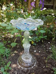 a glass pedestal in the middle of some flowers