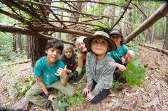 four children sitting on the ground with trees in the background and one child pointing to the camera