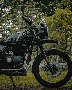 a black motorcycle parked on top of a grass covered field next to trees and bushes