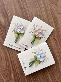 three cards with flowers on them sitting on a table