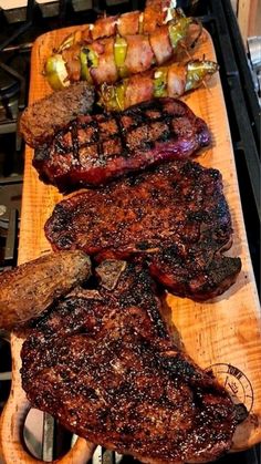 steaks and vegetables on a wooden cutting board next to an open flame oven with tongs