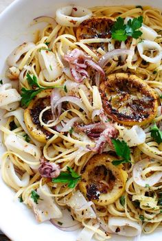 a white bowl filled with pasta covered in onions and meats, garnished with parsley