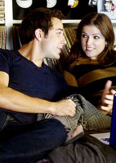 a man and woman sitting on a couch looking at a laptop computer screen while talking to each other