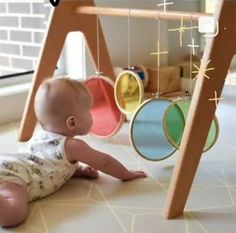 a baby laying on the ground next to a wooden frame with circles hanging from it