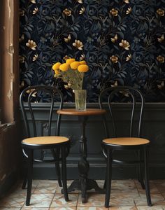 two chairs and a table with flowers on it in front of a floral wallpaper